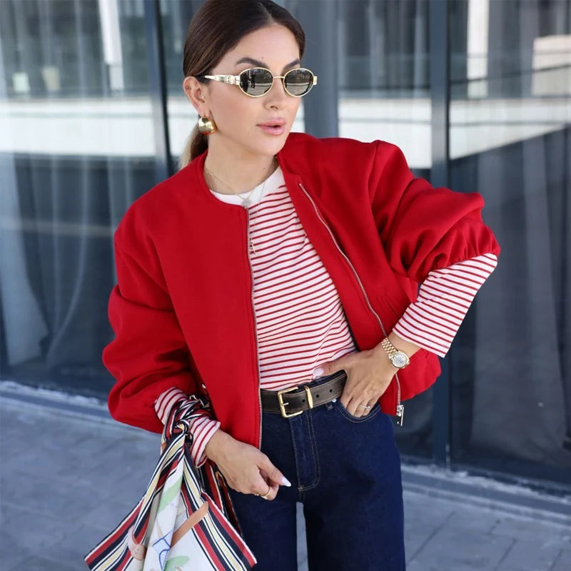 Woman wearing a red jacket, striped shirt, and dark pants outdoors.
