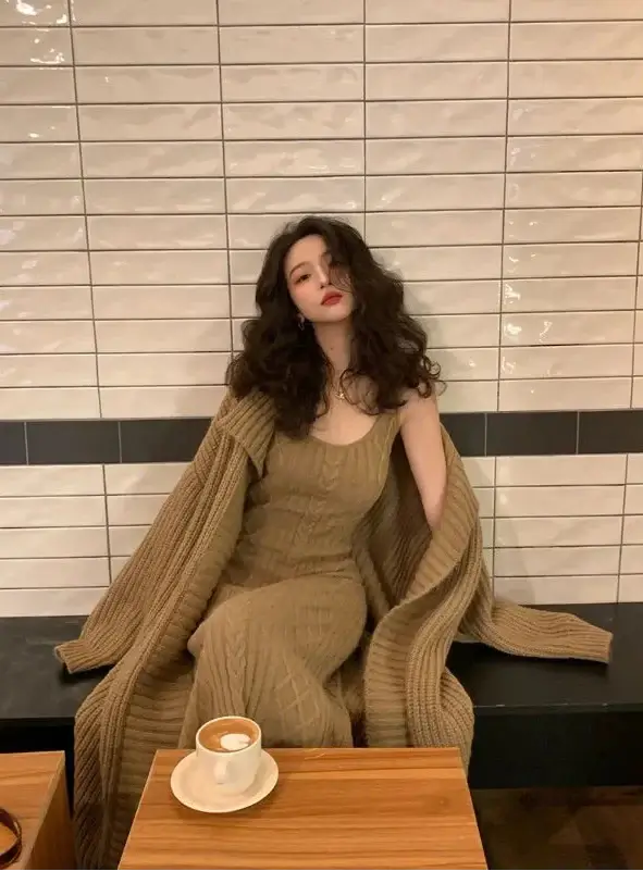 Woman in a green outfit sitting at a table with a cup of coffee against a tiled wall.