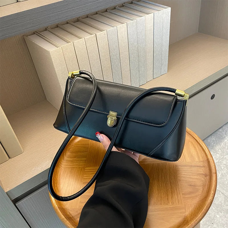 Black handbag with gold accents held by a person on a wooden stool.