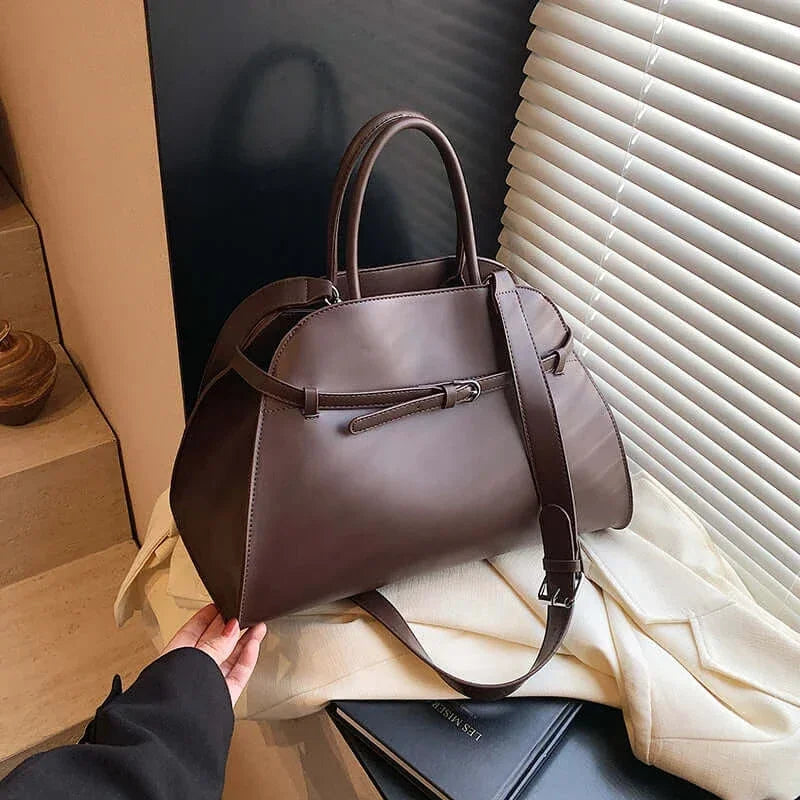 Brown leather handbag on a light-colored surface with a blurred background