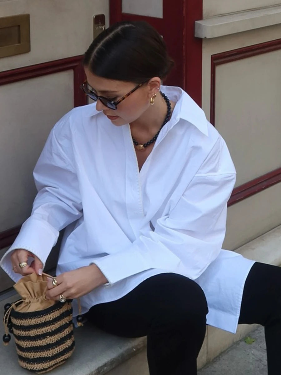 Woman in a white shirt sitting on a bench with a woven bag.