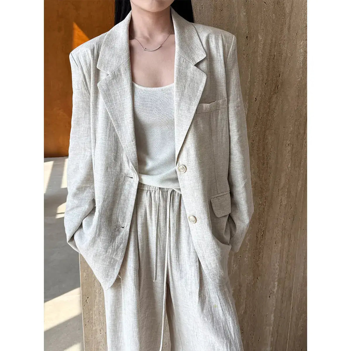 Person wearing a light gray blazer and pants against a wooden background
