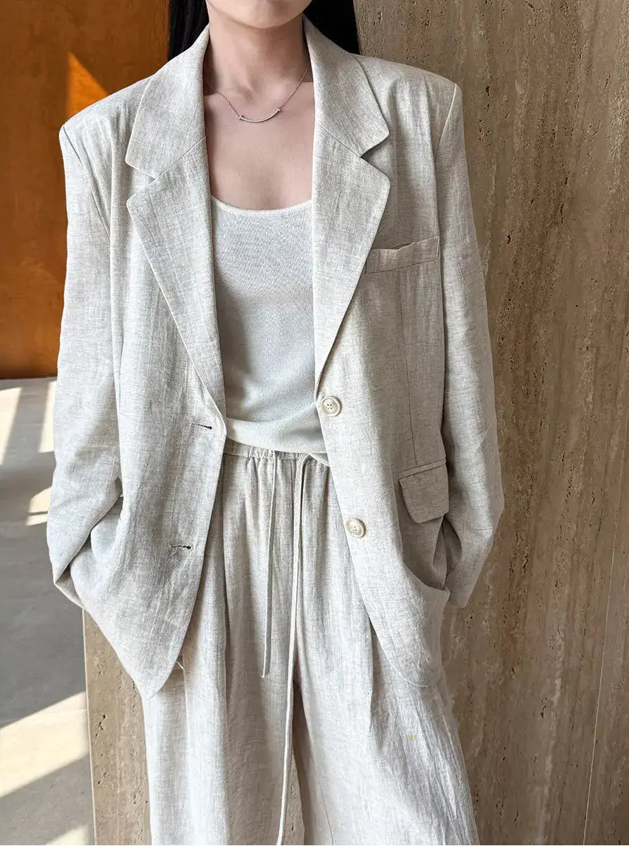 Person wearing a light gray blazer and pants against a wooden background