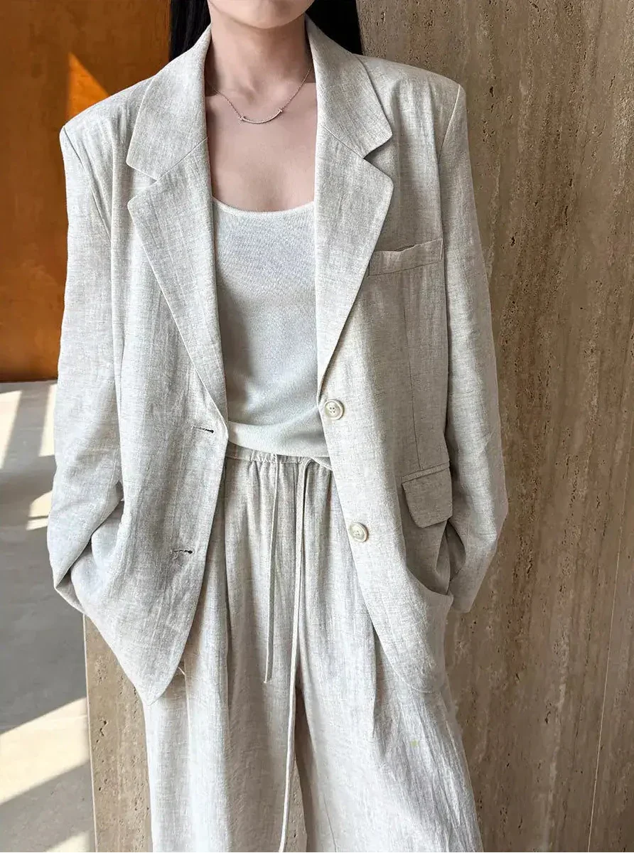 Person wearing a light gray blazer and pants against a wooden background
