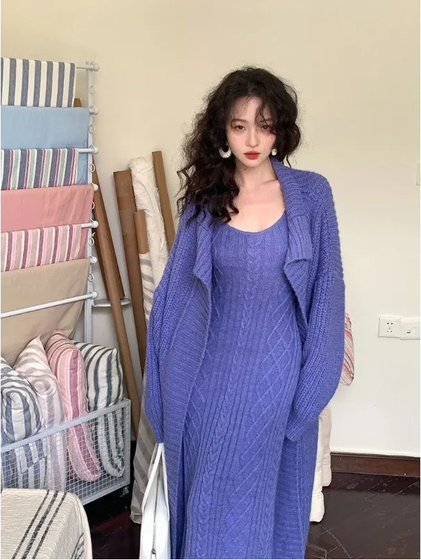 Woman in a blue knit outfit standing next to a rack of folded clothes.