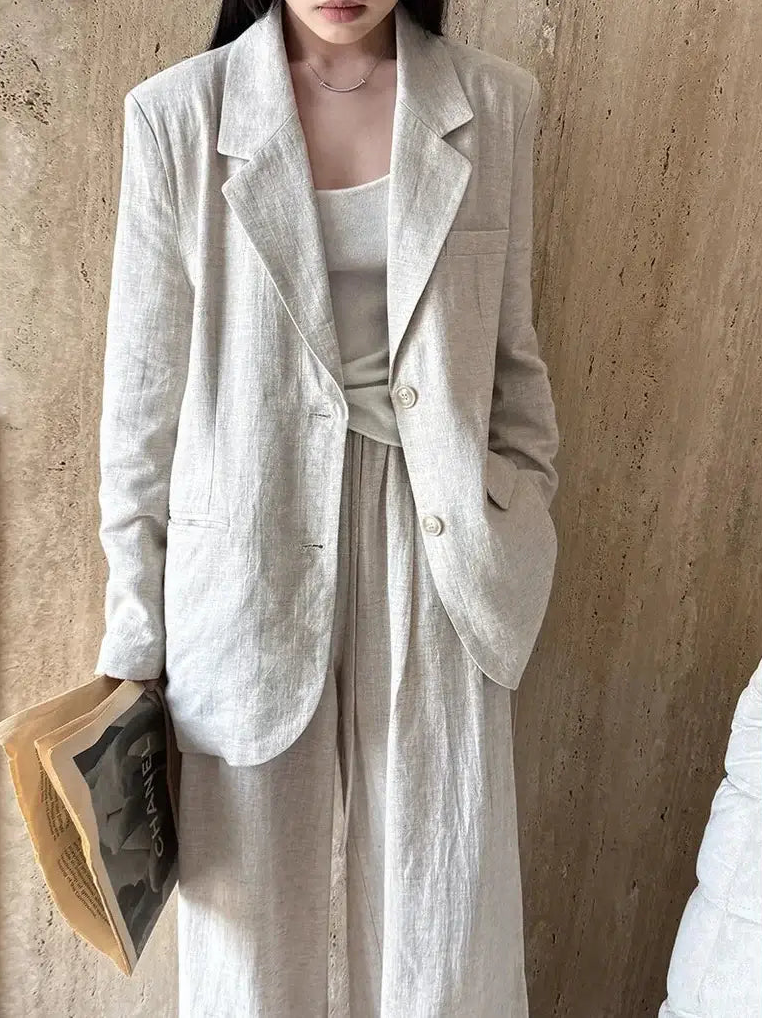 Person wearing a light-colored blazer and dress against a beige wall