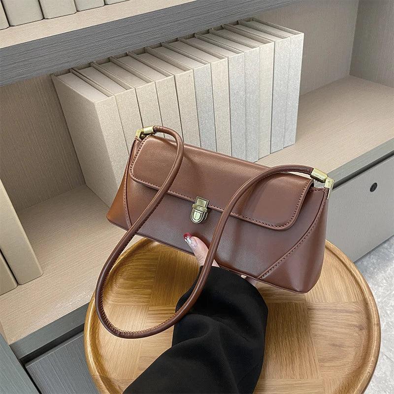 Brown handbag held by a hand on a wooden tray with books in the background