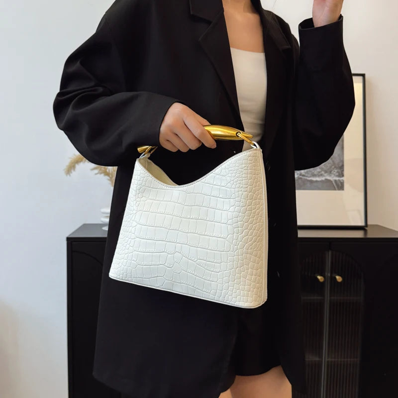 Person holding a white crocodile-patterned handbag with a gold handle.