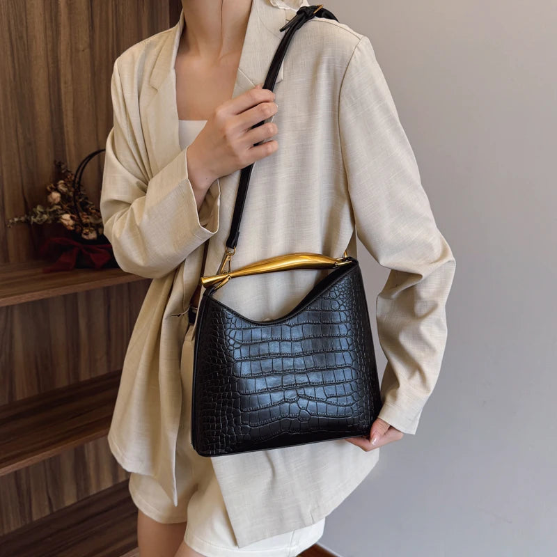 Person holding a black crocodile-patterned handbag with a gold handle.