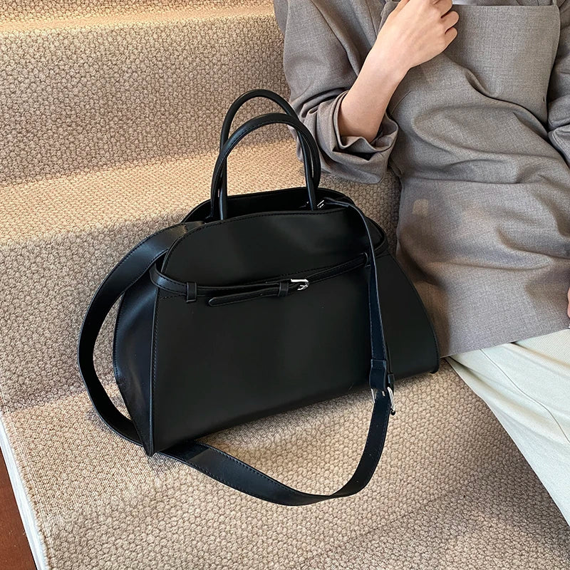 Black handbag on a textured surface with a person sitting in the background
