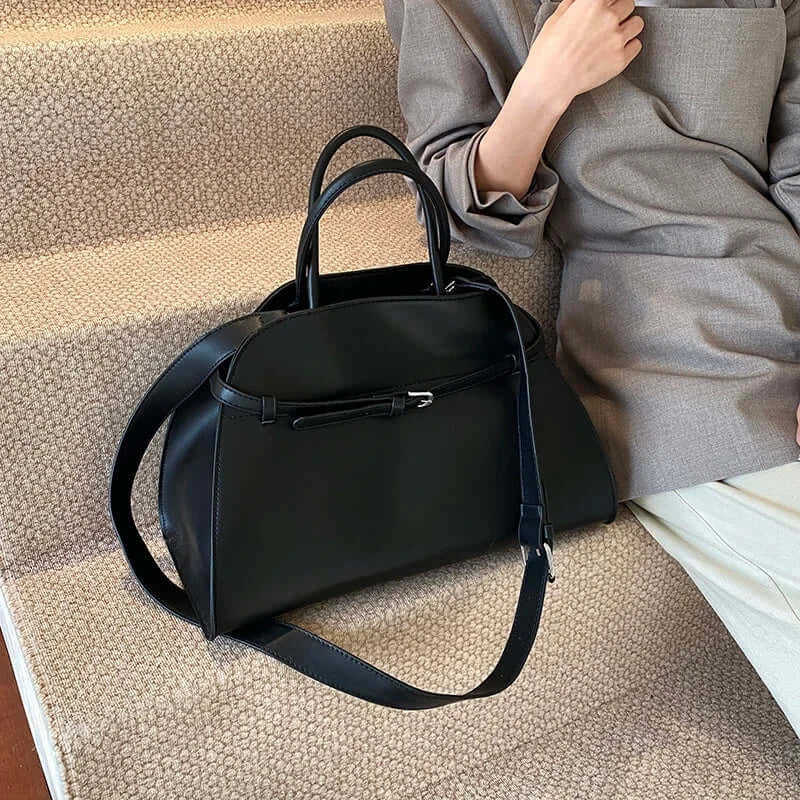 Black handbag on a textured surface with a person sitting in the background