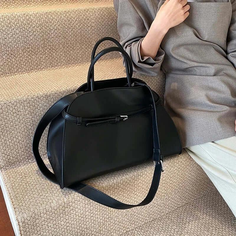 Black handbag on a textured surface with a person sitting in the background