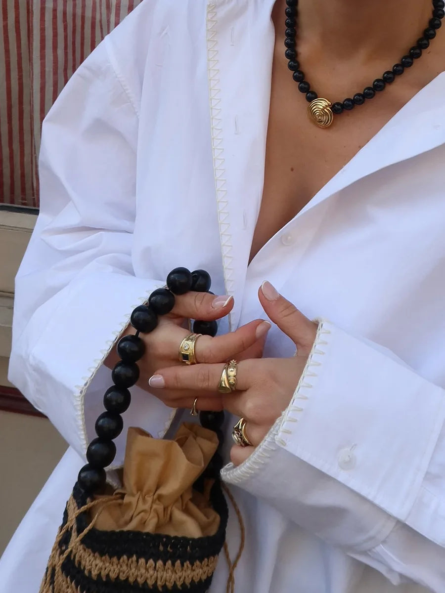 Person wearing a white outfit with gold jewelry and holding black beads.