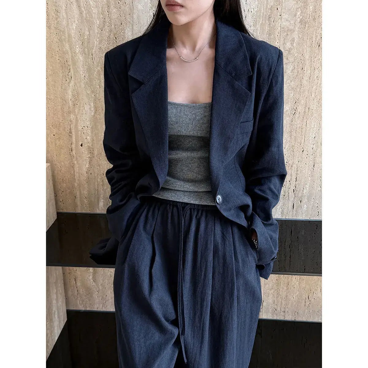 Person wearing a dark blue jacket and pants with a gray top against a wooden wall.