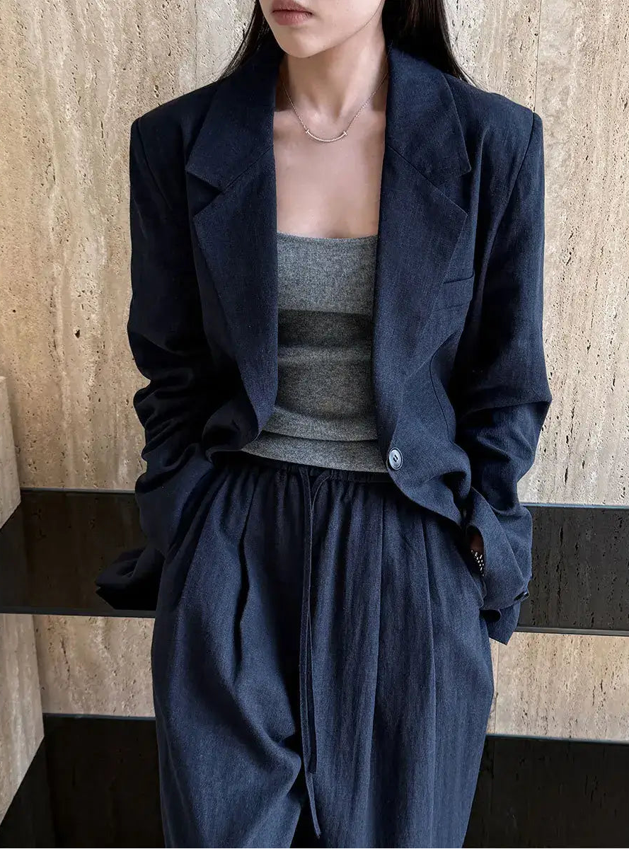 Person wearing a dark blue jacket and pants with a gray top against a wooden wall.
