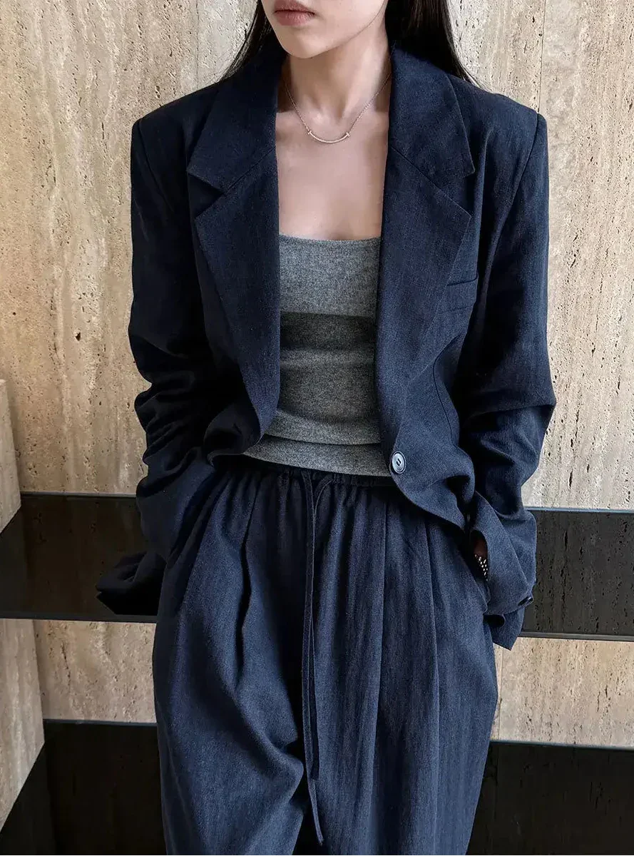 Person wearing a dark blue jacket and pants with a gray top against a wooden wall.