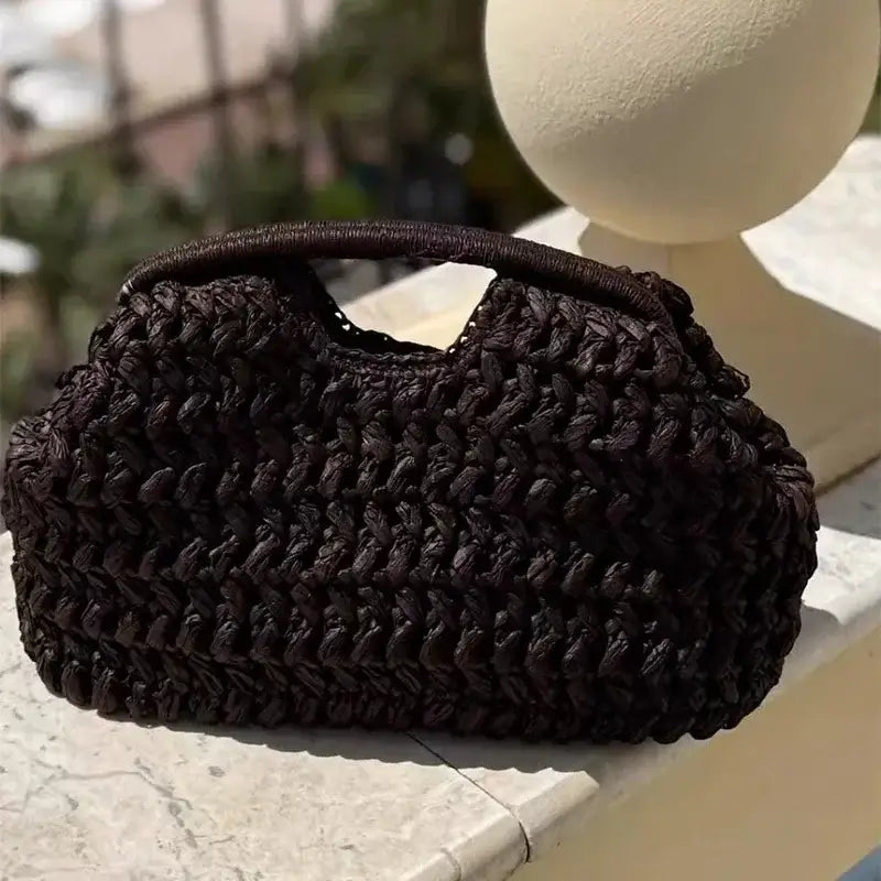 Black woven handbag on a stone ledge with a blurred outdoor background