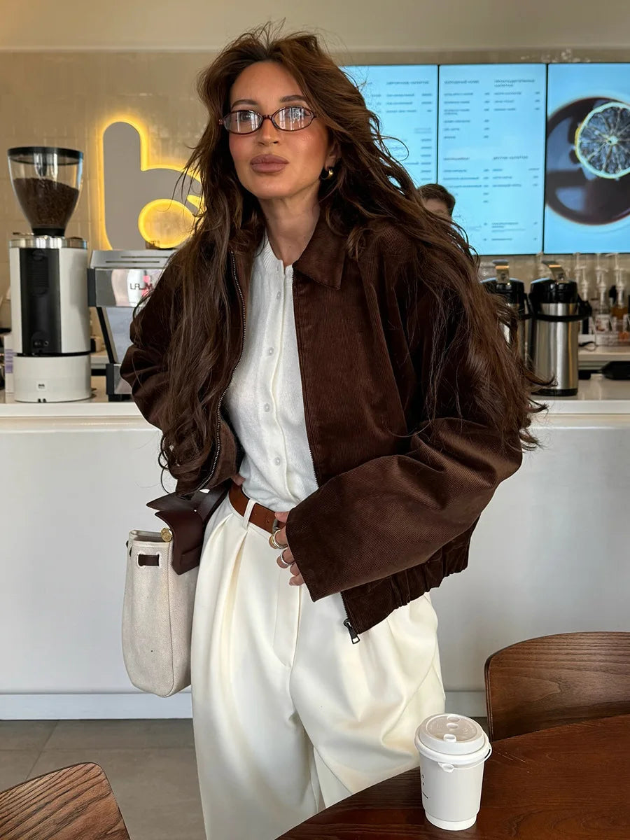 Woman in a brown jacket and white dress standing in a coffee shop.