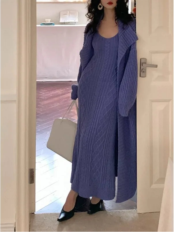 Person wearing a long blue cable knit sweater standing in a doorway.