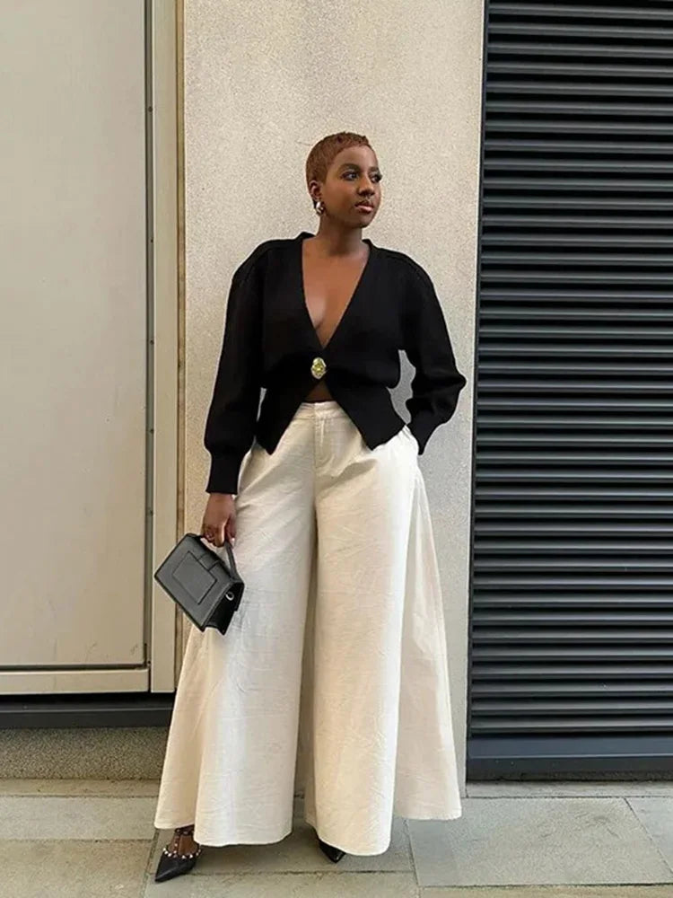Person wearing a black top and white pants standing against a building wall.