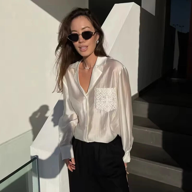 Woman wearing a white blouse with lace details and black sunglasses, standing outdoors.