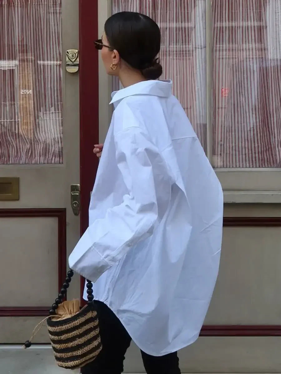 Person wearing a white coat with a textured bag, standing in front of a building entrance.