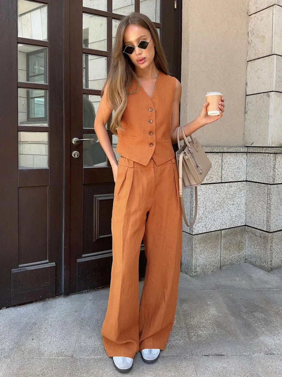 Woman in a brown outfit holding a coffee cup, standing in front of a building.