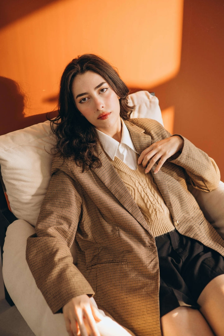 Woman in a brown blazer sitting on a white chair against an orange wall.