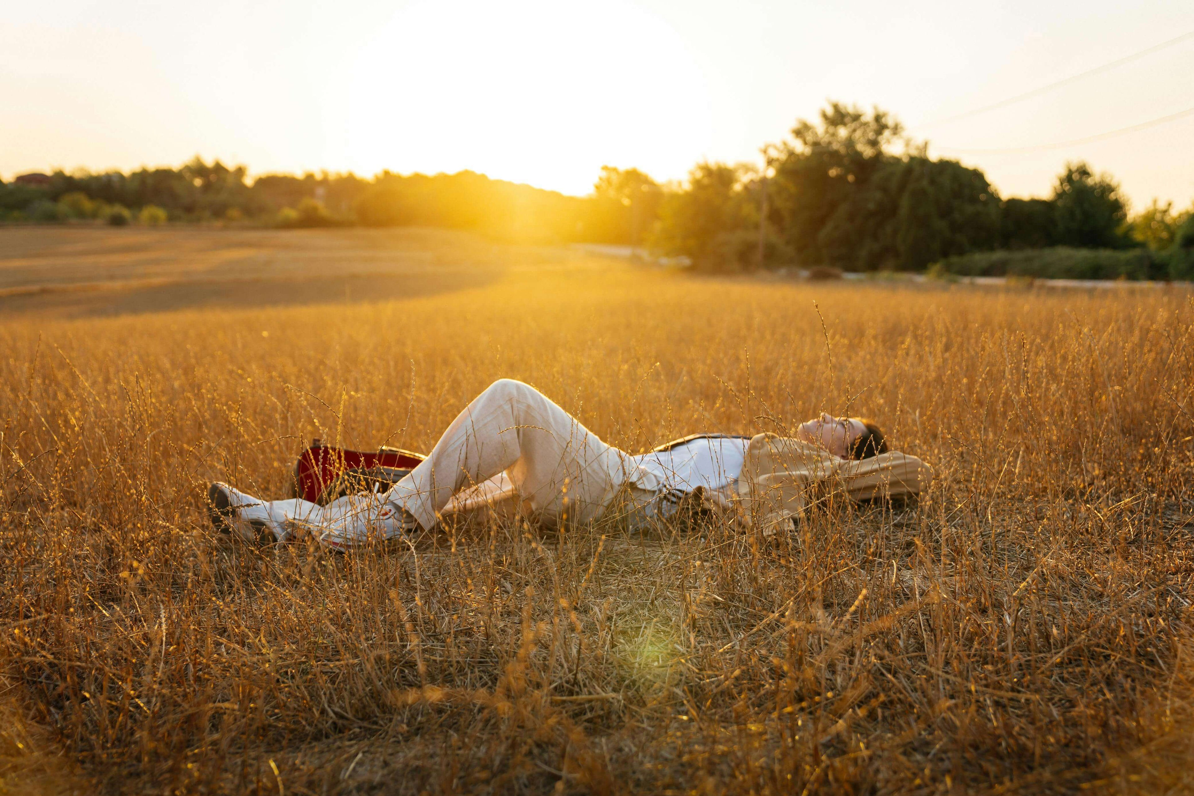 Person lying on a golden field with sunset in the background