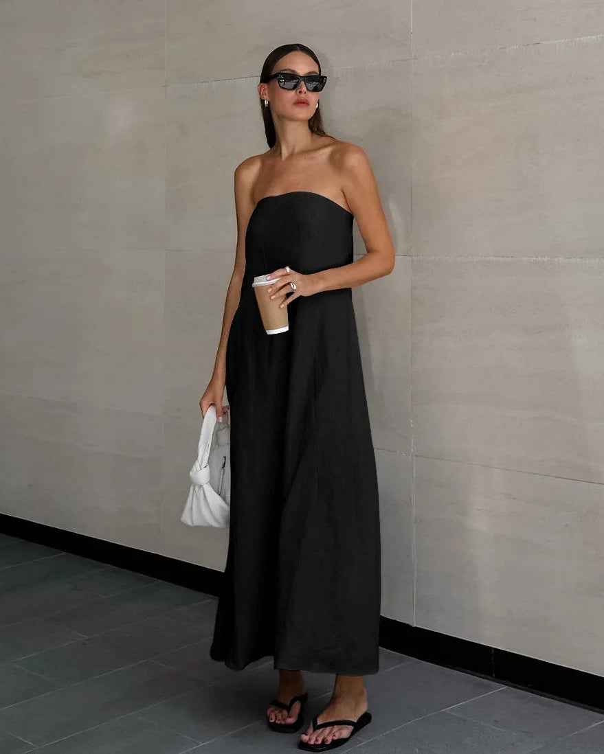 Woman in a black strapless dress holding a white clutch against a neutral wall.