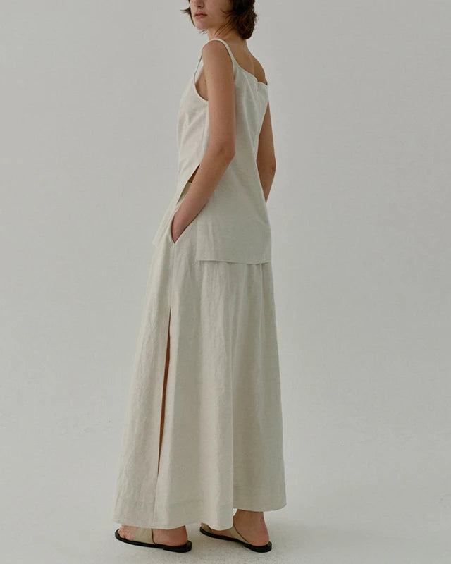 Person wearing a light-colored sleeveless top and wide-leg pants on a plain background
