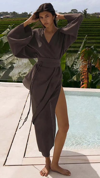 Woman in a gray robe standing by a pool with greenery in the background