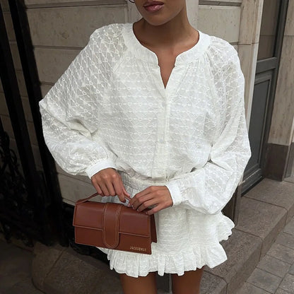 Person wearing a white dress holding a brown handbag on a sidewalk.