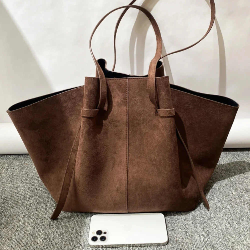 Brown suede handbag on a textured surface with a white background