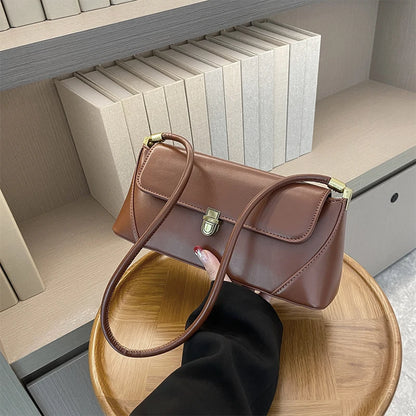 Brown handbag held by a hand on a wooden tray with books in the background
