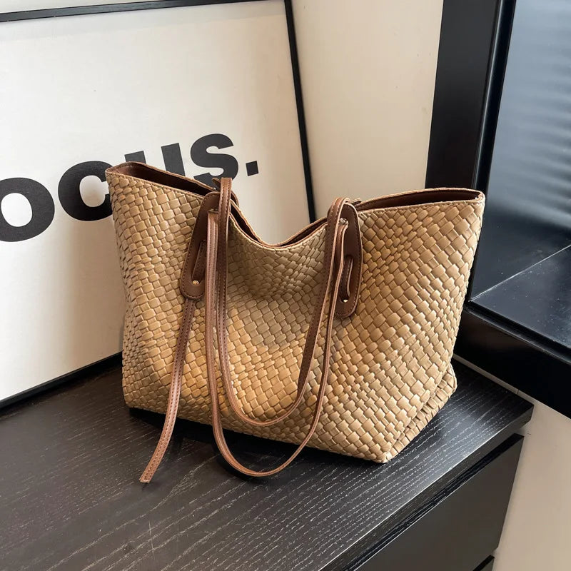 Beige woven handbag with brown straps on a dark surface