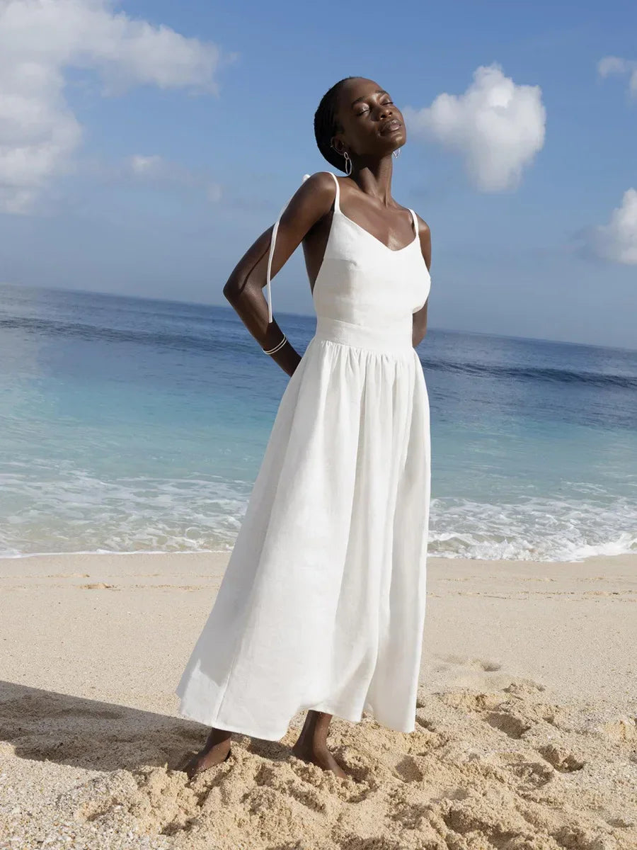 Woman in a white dress standing on a beach with ocean and sky in the background