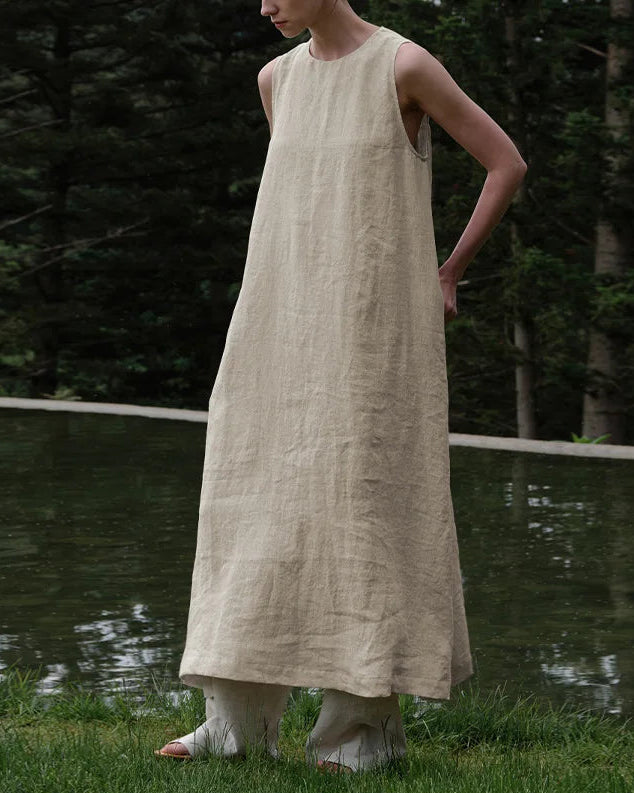 Front view of a woman wearing an elegant sleeveless linen A-line maxi dress in a natural setting.