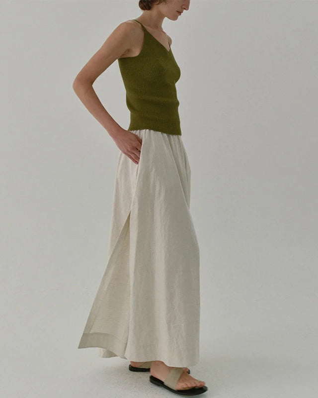 Woman wearing a green top and beige pants on a plain background