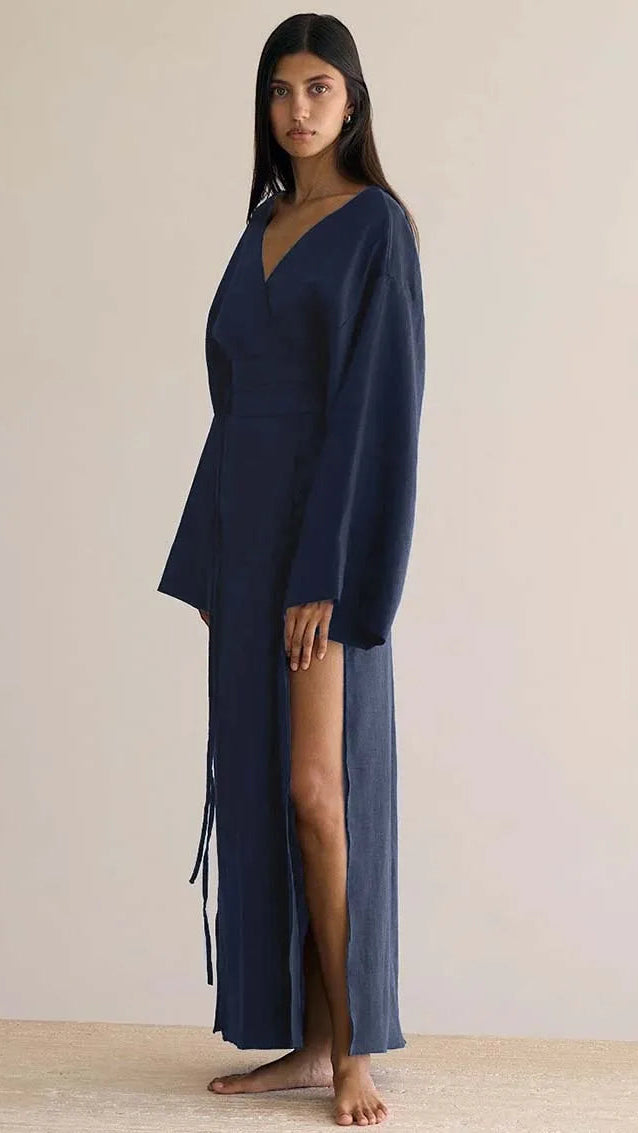 Woman wearing a long navy blue dress with a slit on a plain background