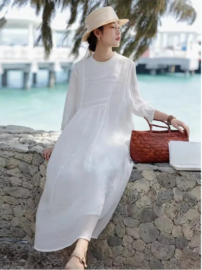 Woman wearing a white pintuck linen-blend maxi dress with 3/4 sleeves and straw hat by the seaside
