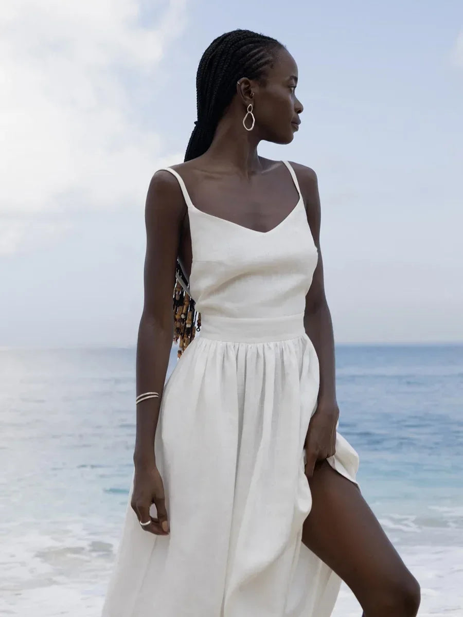Woman in a white dress standing on a beach with ocean and sky in the background