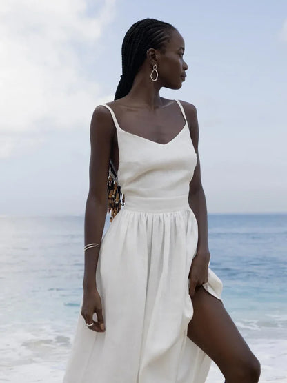Woman in a white dress standing on a beach with ocean and sky in the background