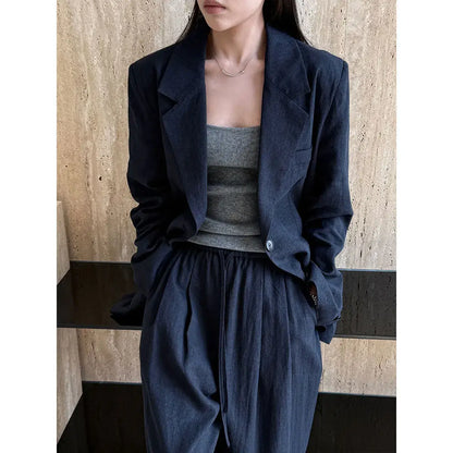Person wearing a dark blue jacket and pants with a gray top against a wooden wall.