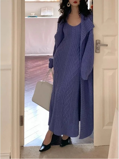 Person wearing a long blue cable knit sweater standing in a doorway.