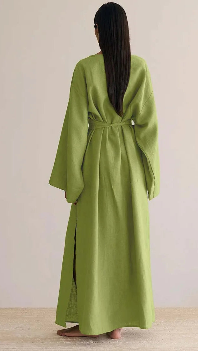 Person wearing a green dress with long sleeves and a belt, standing against a plain background.