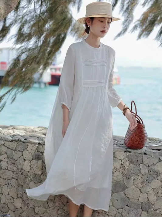 Woman wearing a white pintuck linen-blend maxi dress with 3/4 sleeves and straw hat by the seaside