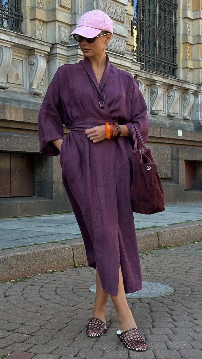 Woman in a purple outfit standing in front of a stone building.