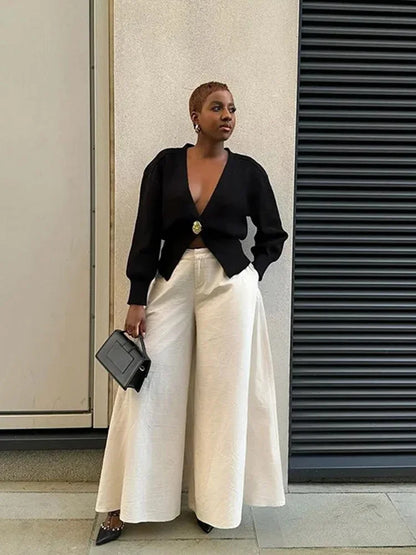 Person wearing a black top and white pants standing against a building wall.