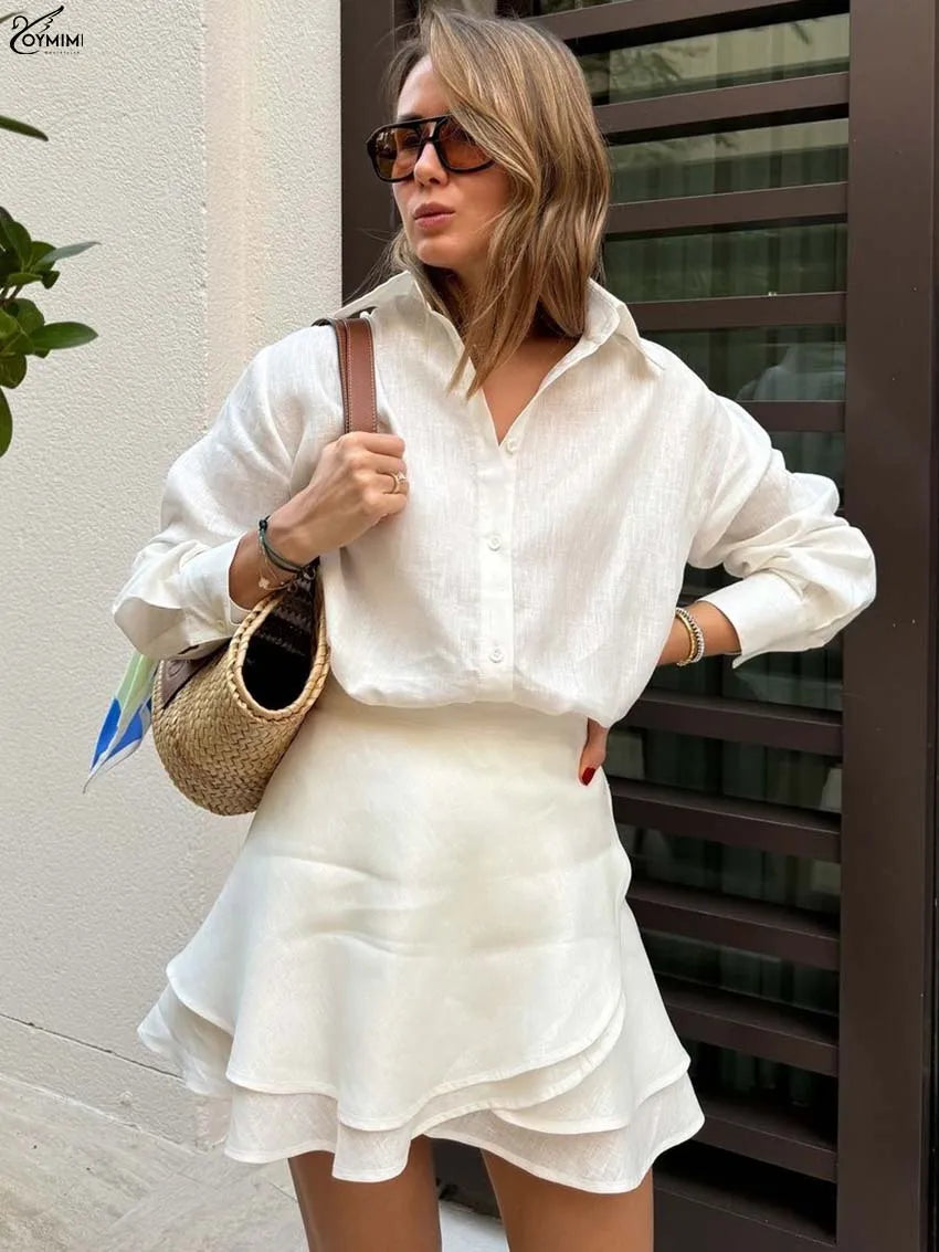 Woman in a white outfit holding a straw bag against a neutral background